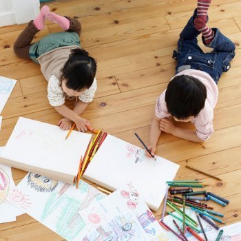 Dos niños dibujando en el suelo vistos desde arriba, mostrando creatividad y expresión emocional en dibujos infantiles